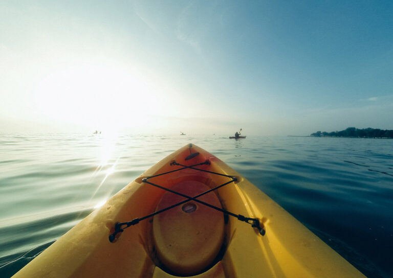 View from a yellow kayak on calm water during sunrise.