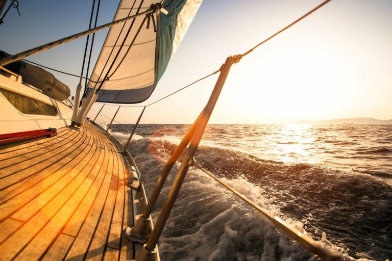 Sailing boat gliding through golden sunset waters.