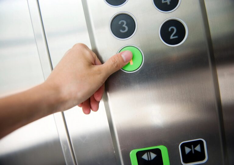 A hand pressing the green elevator button for the first floor.